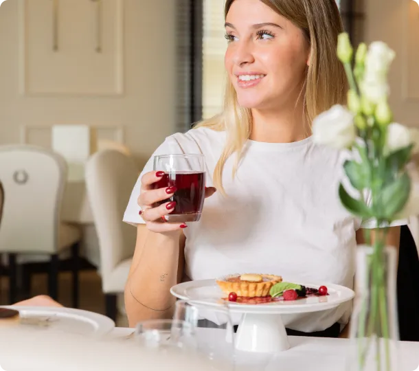 Donna sorridente tiene un bicchiere di succo rosso accanto a un dessert su un tavolo.