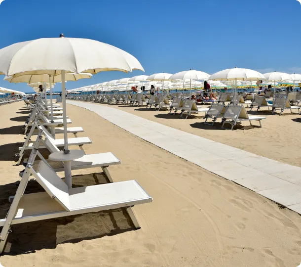 Spiaggia sabbiosa con file di ombrelloni bianchi e lettini sotto un cielo blu.